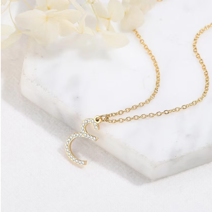 Gold necklace with a heart pendant on a white surface. Arabic Zirconia Initial Necklace. gold, silver, rose gold. Hoop Name Earring gold, sterling silver, rose gold, plated, 18k, makana jewellery, luxury