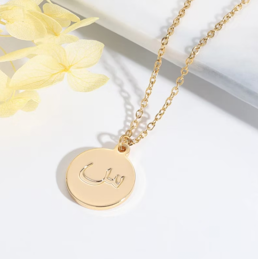 Gold necklace with a round pendant on a white background. Arabic Name Necklace With Stones. gold. rose gold. silver. plated. gold. silver. rose gold. plated 18k solid sterling silver. makana jewellery jewelry