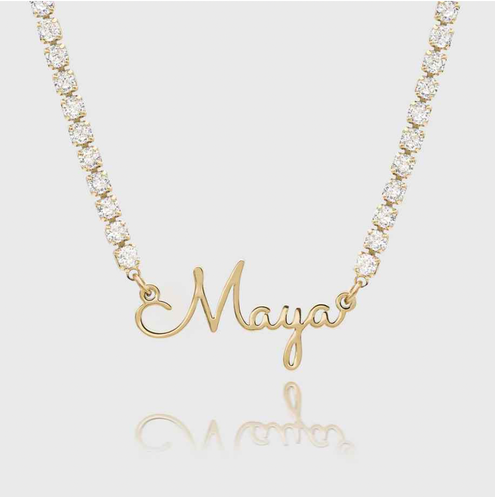 A gold nameplate necklace spelling 'Maya' in cursive script, hanging from a gold chain adorned with clear round-cut stones. Sterling Silver Finish / 18k Gold Plated / 18k Rose Gold Plated / 18k white Gold Plated / 22k Gold Plated. Makana jewellery, jewelry