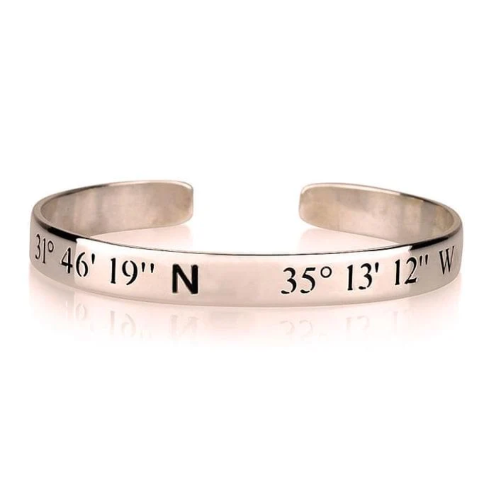 A silver metal cuff bracelet engraved with geographical coordinates, including '31° 46' 19" N' and '35° 13' 12" W', gold plated, sterling silver 925, rose gold plated, imitation jewellery, Makana Jewellery, 18k, jewelry