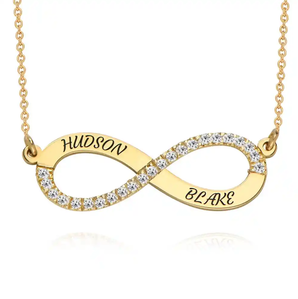 A gold infinity necklace with clear pavé stones along the lower curve and the names. Diamond, sterling silver 925, gold plated, rose gold plated. makana jewellery, jewelry